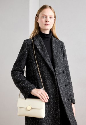 Fekete-fehér houndstooth mintás gyapjú kabát, dupla gombolású kialakítással, amelyhez egy krémszínű táska tartozik, kerek arany fémzárral.