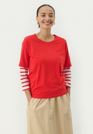 Red short-sleeve top combined with white and red striped long sleeves; soft fabric; casual design; paired with a beige skirt.