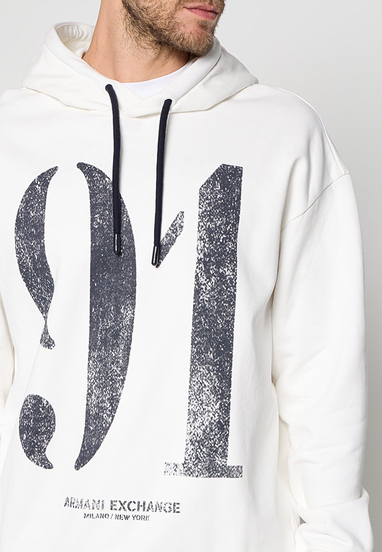 Hombre vistiendo una sudadera blanca con una gran impresión desgastada en negro "9/1" y el texto "Armani Exchange Milano/New York" debajo.