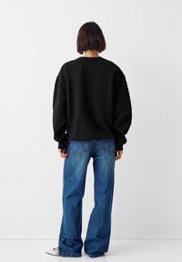 Sudadera negra de gran tamaño con escote redondo, combinada con jeans de mezclilla de cintura alta en un tono azul claro, que tienen un ajuste relajado y bolsillos traseros.