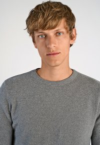 Maglione grigio texturizzato con collo rotondo, caratterizzato da un motivo sottile. Il materiale sembra morbido, aderendo strettamente al corpo.