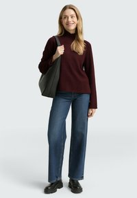 Bordeaux, hoge nektrui gecombineerd met wijde blauwe denim jeans en zwarte laarzen met dikke zool, aangevuld met een grijze schoudertas.