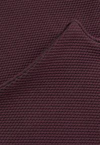 Bordeaux textiel met een geweven patroon, dat een zachte, tactiele oppervlakte en een gevouwen rand met contrasterend stiksel toont.