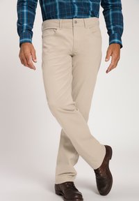 Pantalones de algodón beige con un diseño de pierna recta, bolsillos frontales y cierre de botón, combinados con zapatos de cuero marrón oscuro.
