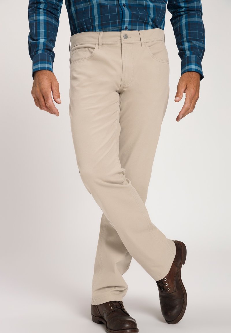 Pantalones de algodón beige con un diseño de pierna recta, bolsillos frontales y cierre de botón, combinados con zapatos de cuero marrón oscuro.