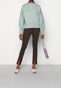 Hellgrüner, übergroßer Pullover, braune, enganliegende Hose mit Seitenschlitzen und blassrosa, offen-toed Mules. Lila Handtasche mit Kettenriemen.