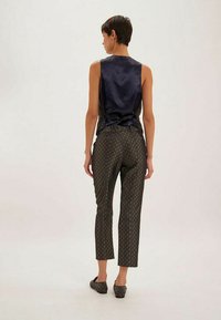 Haut sans manches en satin marine avec un nœud à l'arrière, associé à un pantalon court marron à motifs arborant un design géométrique, porté avec des chaussures sombres.