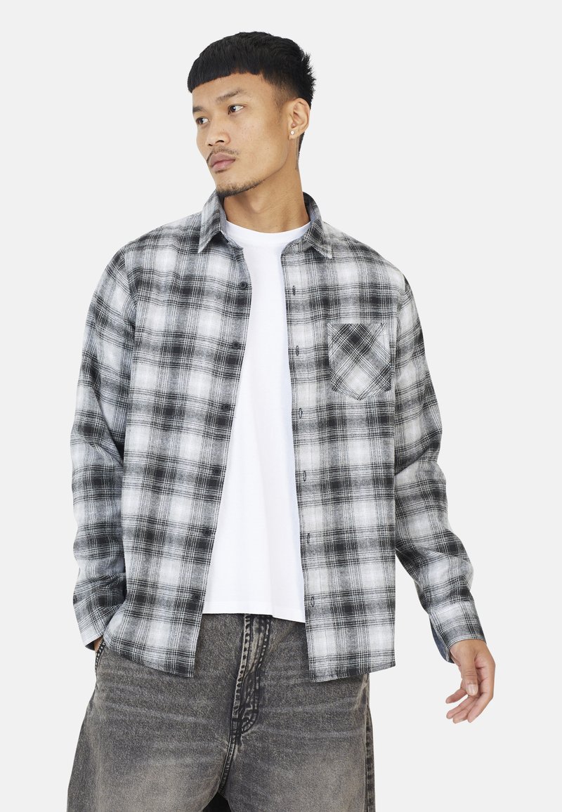 Zwart-wit geruite flanellen shirt met knopen en een borstzak, gedragen over een wit T-shirt; de stof lijkt zacht en gestructureerd.