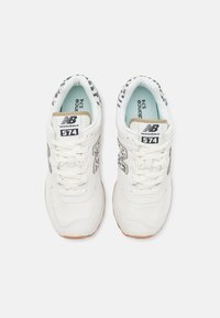 Ζευγάρι λευκών αθλητικών παπουτσιών New Balance 574 με λεπτομέρειες σε μοτίβο λεοπάρ στα πλάγια και γύρω από το γιακά, σε θέα από πάνω.