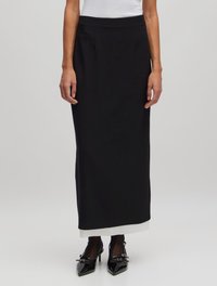Zwarte zwijgende rok van vloerlengte, gemaakt van gladde stof met een aansluitende tailleband. Beschikt over een contrasterende witte zoom. Gemaakt met puntige zwarte schoenen.