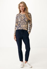 Pantalones jogger azul marino combinados con una camiseta de manga larga beige que presenta un patrón de rayas de cebra azul. Zapatillas blancas completan el conjunto.