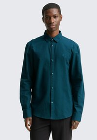 Teal overhemd met knopen, gemaakt van een zachte stof met een subtiele textuur, voorzien van een kraag, lange mouwen en een klein logodetail op de borst.