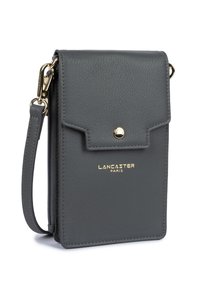 Grijze leren schoudertas met gouden hardware, klep sluiting en gegraveerd logo. Compact ontwerp met een polsband en ritsvak.