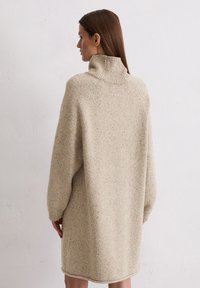 Beiges Strickkleid mit hohem Rippkragen, oversized Ärmeln und einer gemütlichen Textur. Der Saum reicht bis über die Oberschenkelmitte und hat Rippdetails.
