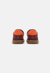 Lädersneakers med en djup burgundyröd ovandel, orange hälaccenter och en flexibel brun sula. Slät textur med minimal logotyp på baksidan.