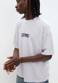 Gray short-sleeve t-shirt with a crew neckline, featuring a rectangular logo in multicolored text on the chest. Soft, textured fabric.