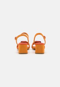 Sandali con tacco a blocco in suede arancione con cinturini alla caviglia regolabili, apertura sul retro e fodera interna rosa a contrasto, caratterizzati da una texture liscia.