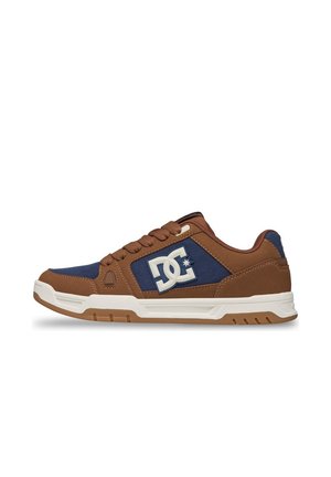 Baskets basses marron et bleu marine avec semelle blanche et logo DC sur le côté, montrant le profil gauche sur fond blanc.