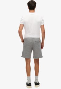 Pantalones cortos de algodón gris con cintura elástica, bolsillos laterales y un bolsillo trasero. Combinados con una camiseta blanca de manga corta y zapatillas negras.
