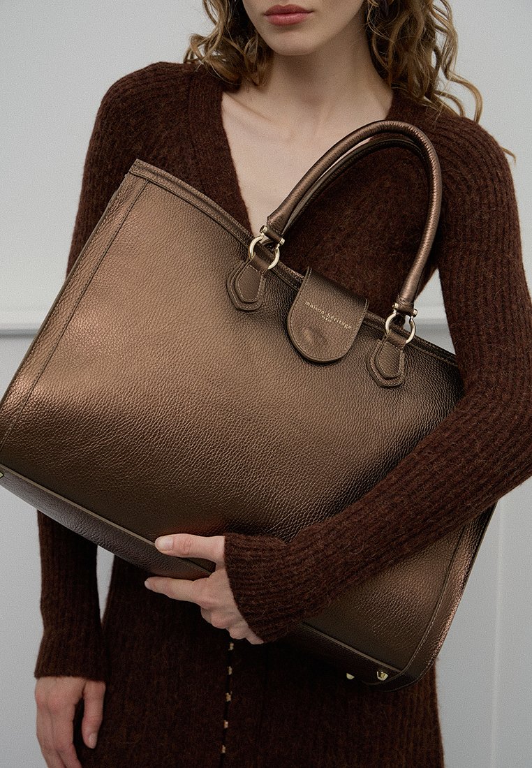 Sac fourre-tout en cuir bronze métallique avec finition texturée, double poignées et fermeture à rabat. Bord lisse et accents de quincaillerie subtils.
