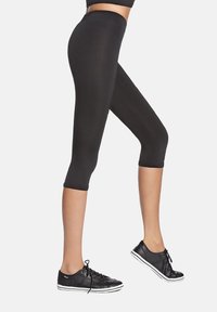 Czarne legginsy capri wykonane z elastycznego materiału, z wysokim stanem i dopasowanym krojem, zestawione z czarnymi trampkami.