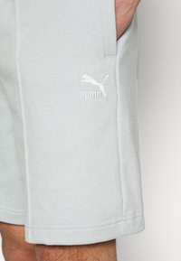 Svetlomodré bavlnené šortky s elastickým pásom, bočnými vreckami a bielou vyšitou logom Puma na ľavom stehne.
