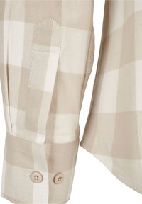 Poignet de chemise à manches longues à carreaux beige et blanc avec deux boutons beiges et détails visibles de la patte de boutonnage cousue.
