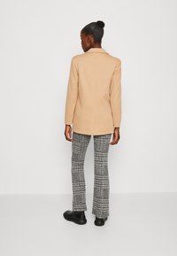 Beige skreddersydd blazer og mønstrede klippede bukser, med et teksturert strikk i svart og hvitt. Svarte ankelstøvler fullfører antrekket.