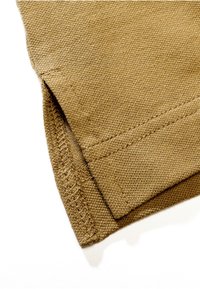 Gros plan d'un tissu en coton beige montrant la couture détaillée de l'ourlet et le bord plié sur un fond clair.