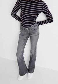 Un suéter de cuello alto a rayas blancas y negras combinado con unos pantalones vaqueros acampanados grises. Modelo vistiendo zapatillas blancas. Diseño simple y ajustado con acentos mínimos.