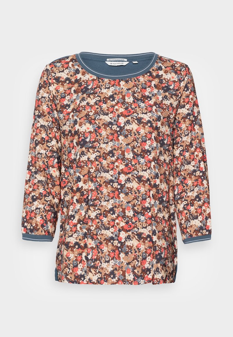 Camicia a fiori con maniche 3/4, scollatura tonda e polsini a contrasto. I colori includono marrone, blu navy, rosso e crema. Tessuto leggero.