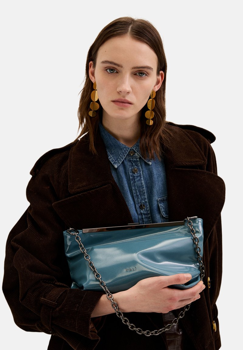 Tyrkysová lakovaná kabelka s řetízkem, která se vyznačuje hladkým povrchem a jemně zmačkaným designem. Kovové detaily na vrchu.