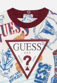 Λευκό βαμβακερό T-shirt με μαρονο κόψιμο στο λαιμό, πολύχρωμα ναυτικά σχέδια και ένα εμφανές μαρονο τρίγωνο λογότυπο με την ένδειξη "GUESS U.S.A."