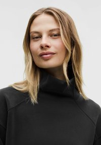 Zwarte sweatshirt met hoge kraag, zachte textuur en naaddetails. Heeft een losse pasvorm en een minimalistisch ontwerp.