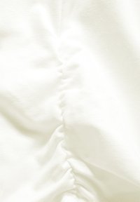 Tessuto bianco con una consistenza morbida, caratterizzato da dettagli arricciati su un lato, creando un lieve effetto drappeggiato.