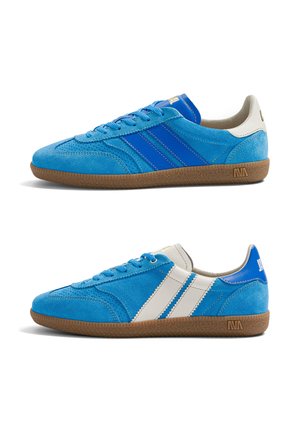 Deux baskets basses en daim bleu avec des semelles marron, l'une avec des rayures bleues et l'autre avec des rayures blanches sur les côtés.