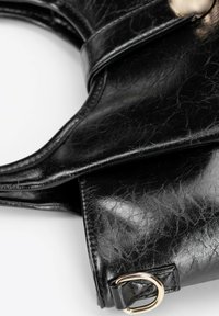 Sac en cuir synthétique noir avec une finition brillante, un design courbé et un accent en matériel doré. Surface texturée avec des plis visibles.