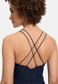 Granatowa sukienka z krzyżującymi się ramiączkami, dopasowanym gorsetem i ukrytym zamkiem z tyłu, wykonana z gładkiego materiału.