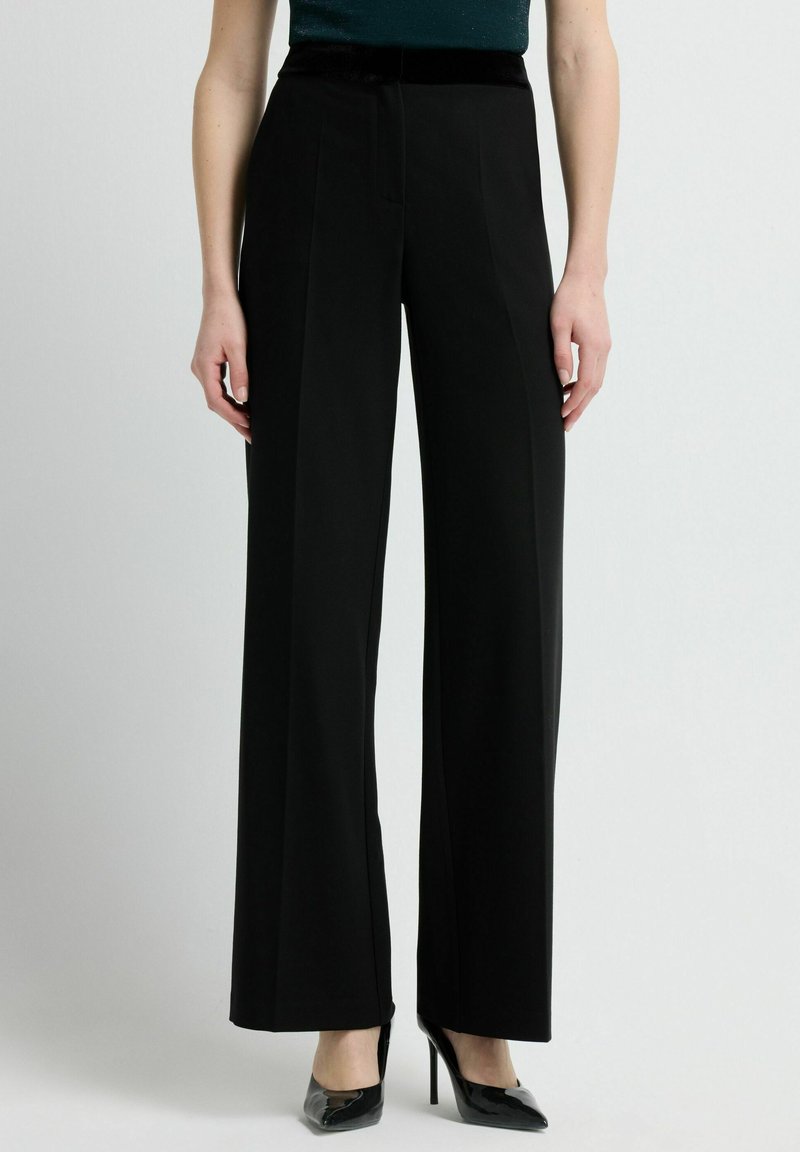 Zwarte wijde broek met een gladde textuur, voorzien van een fluwelen tailleband. Getailleerde pasvorm met voorplooien en een scherpe afwerking.