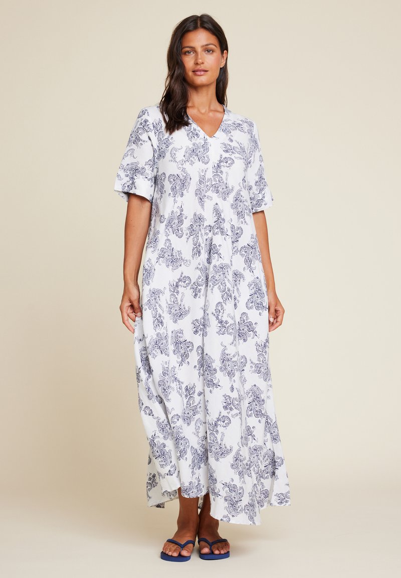 Maxikjole i hvitt stoff med blå paisleymønster, V-hals, korte ermer og en avslappet passform. Kombinert med marineblå flip-flops.