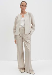 Beige cropped jack gemaakt van zachte stof, gecombineerd met lichtbeige wijde broeken en crèmekleurige instappers met een gestructureerd detail.