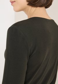 Maglia verde scuro a maniche lunghe vista da dietro, con una texture liscia, scollo rotondo e silhouette aderente, con cuciture sulle spalle visibili.