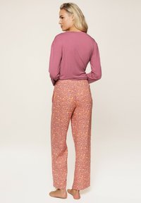 Langærmet mauve top parret med løstsiddende, mønstrede bukser i orange og pink med leopardmønstret design. Blød stoftekstur.