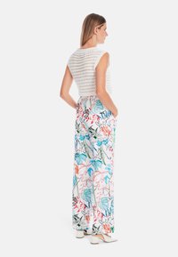 Weiße gehäkelte Bluse mit taillierter Form, kombiniert mit weitläufigen Hosen, die bunte Blumenmuster auf einem hellen Hintergrund zeigen.