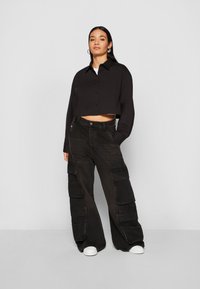 Black cropped button-up shirt with long sleeves, paired with wide-leg black cargo pants featuring multiple large pockets. White sneakers.