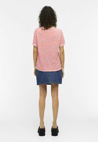 T-shirt rayé rouge et blanc à manches courtes, associé à une jupe en denim. La tenue comprend des chaussures plateformes noires épaisses.