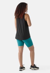 Top nero senza maniche con una vestibilità ampia, abbinato a pantaloni corti compressivi turchesi. Scarpe da ginnastica nere con dettagli bianchi, tessuto testurizzato.