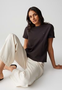Zwarte katoenen T-shirt met opgerolde mouwen, voorzien van een klein hartlogo. Gecombineerd met losse, crèmekleurige broeken. Glad stoffen textuur.