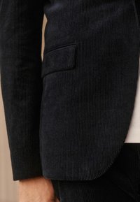 Black corduroy blazer with a textured surface, featuring a single chest pocket, and a straight-cut design.