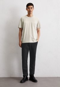 Lichtgroene T-shirt met korte mouwen en geborduurd logo, gecombineerd met donkergrijze broek en zwarte veterschoenen. Eenvoudig, modern ontwerp.